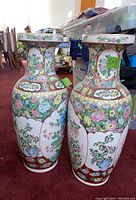 Pair of tall Asian hand-painted porcelain vases on a carpeted floor with floral designs and wide flared tops.