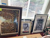 Overall view of three framed art pieces leaning against a window ledge. Two paintings and one photo print visible.