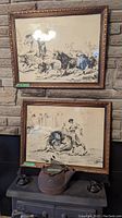 Two framed charcoal art pictures on a wall and antique cast iron kettle placed on a stove.
