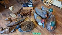 Overview photo showing 12 wooden carved birds including 3 decoys, a boot brush duck with bristles, and several other bird figurines on wooden table.