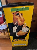Left side view of the Camel metal ashtray showing cartoon camel in tuxedo with Camel cigarette pack and 'The Hard Pack' branding.