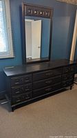 Photo of the full dresser with mirror mounted on wall behind it, showing the front and top surfaces of the dresser and the mirror overall.