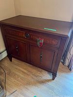 Angled front view of wooden cabinet showing burl veneer drawer, Gibbard Craftsmen badge, and brass hardware.
