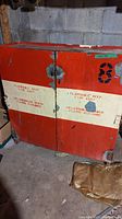 Front view of red metal flammable storage cabinet with beige stripe and stenciled black text and number 8 on doors.