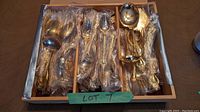 Set of gold plated cutlery items arranged in tray with plastic wrapping.