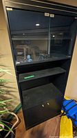 Black shelving cabinet with glass doors and lights, tall with shelves and a lower storage cupboard.
