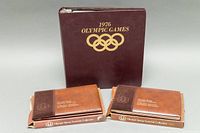 Three binder-style Olympic Stamp Souvenir Collections with original boxes, one large dark burgundy and two smaller brown volume folders.