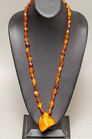 Full view of 28-inch amber bead necklace displayed on a black bust with the large pendant front and center.