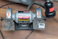 Front view of the CRAFTSMAN 6" bench grinder showing model and warning labels, dual grinding wheels with protective shields, and attached flexible work light.