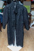 Front view of long black Persian lamb fur coat on dress form, showing curly textured fur with full sleeves and collar.
