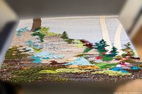 Full view of vintage knit wall hanging laid flat showing nature landscape design with trees, water, and rocks.
