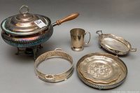 Full view of chafing pot with lid and wooden handle, handled cup, round riser, and two trays on a neutral surface