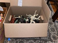 Open cardboard box containing multiple assorted vintage horror-themed plastic action figures including mummies, Frankenstein's monsters, and others.