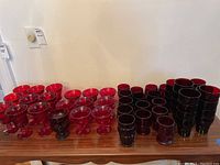 Photo showing multiple red glass goblets and dark water glasses arranged on table