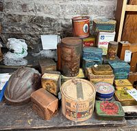 Photo showing assortment of vintage metal tins including large cylindrical Prince Albert and Square Edgeworth tins with visible rust and wear. Additional small tins including a metal dome-shaped container and various square and rectangular tins.
