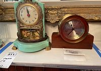 Two mantel clocks on display together, showing ornate vintage clock with mint green base and Howard Miller clock with brass bezel and wooden base.