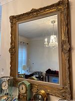 Framed mirror reflecting a chandelier and part of a room with clocks in the foreground.
