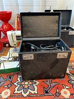 Black hinged case open showing a folded Singer sewing machine inside with power cord