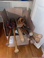 Box showing multiple wooden baseball bats and baseball gloves inside with some gloves resting on top