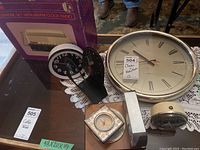 Photo showing assortment of seven clocks including large oval wall clock, black and cream alarm clocks, compact travel clock, and telephone clock radio in box.