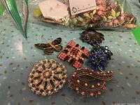 Various colorful costume jewelry brooches placed on a surface including floral and paisley designs with rhinestones.
