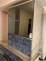 Front angle view of the wood dresser showing the two blue-grey material covered drawers with metal handles and mirrored doors above.