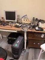 Photo of table with multiple phones, computer monitor, power bars, and black computer tower on floor beneath.