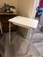 White adjustable plastic TV table with rectangular surface and tubular legs.