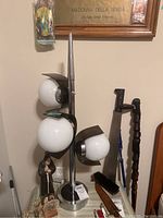 Front side view of MCM table lamp showing three white globe bulb covers with dark plastic shields and metal base standing approximately 34 inches tall.