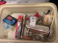 Photo showing assembled meat grinder with wooden handle, funnel, screwdriver in packaging, and additional small parts in container.