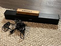 Soundbar, power adapter, audio cable and boxed mount bracket arranged on floor mat