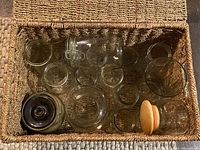 Top view showing a collection of glass jars of different sizes, shapes, and styles in a woven basket.