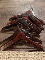 Photo showing a stack of wooden clothing hangers with metal hooks, various shades of wood from reddish to dark brown.