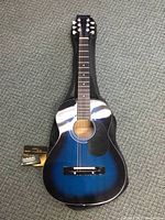 Full view of blue Denver acoustic guitar laid on top of a soft black padded bag with clip-on tuner attached.