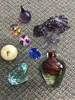 Photo of all eight glass pieces grouped on carpet including bird sculpture, owl figurine, several faceted paperweights, and vase-shaped glass piece.