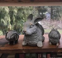 Three resin bunny sculptures displayed on a wooden surface with forest background, showing large, medium, and small sizes.