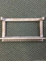 Full view of rectangular wooden frame with chicken wire center and six metal hooks on bottom bar for jewelry hanging.