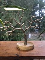 Side view of the metal tree jewelry display on a wooden base placed on a wooden surface with a natural background.