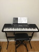 Front view of the keyboard on stand with padded stool below and music sheet on holder.