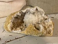 Front angle showing hollow interior lined with sparkling white quartz crystals and rough beige outer surface.