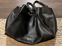 Front view of Nine West black leather tote handbag lying on floor.
