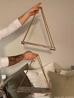 Pair of hanging shelves made from solid wood planks suspended by thick natural fiber ropes. Shown held by hands against a wall background to illustrate size and hanging style.