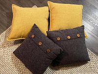Four decorative pillows on woven rug, two yellow and two dark gray with button detail