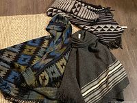 Photo showing all three woven blanket ponchos arranged on floor, showcasing varied patterns and colors.