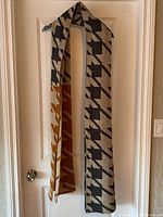 Full view of long knit scarf displaying large houndstooth pattern in black and beige hanging on door.