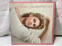 Front cover of Olivia Newton-John's Greatest Hits Vol. 2 showing artist lying with arms raised, wearing a white knitted sweater.