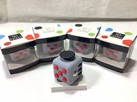 Four new boxed light gray fidget cubes with red buttons displayed with one cube out of the box.