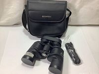 Binoculars with case and strap laid out flat on white surface.