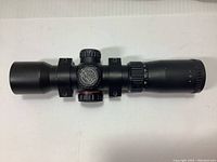 Top view of matte black Excalibur Tact 100 crossbow scope with mounting rings attached, showing adjustment turrets with markings.