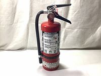 Front view of the red 5lbs ABC dry chemical fire extinguisher showing the cylinder, handle, pin, and hose attached.
